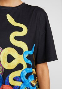 Black t-shirt featuring an illustration of colorful snakes in yellow and blue, with a textured finish and relaxed fit.