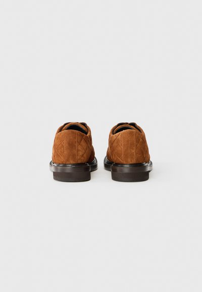 Bruna mockaskor med kviltad textur, minimal sömnad och en slät, mörk gummisul. Har en rundad tå och är utan baksida.