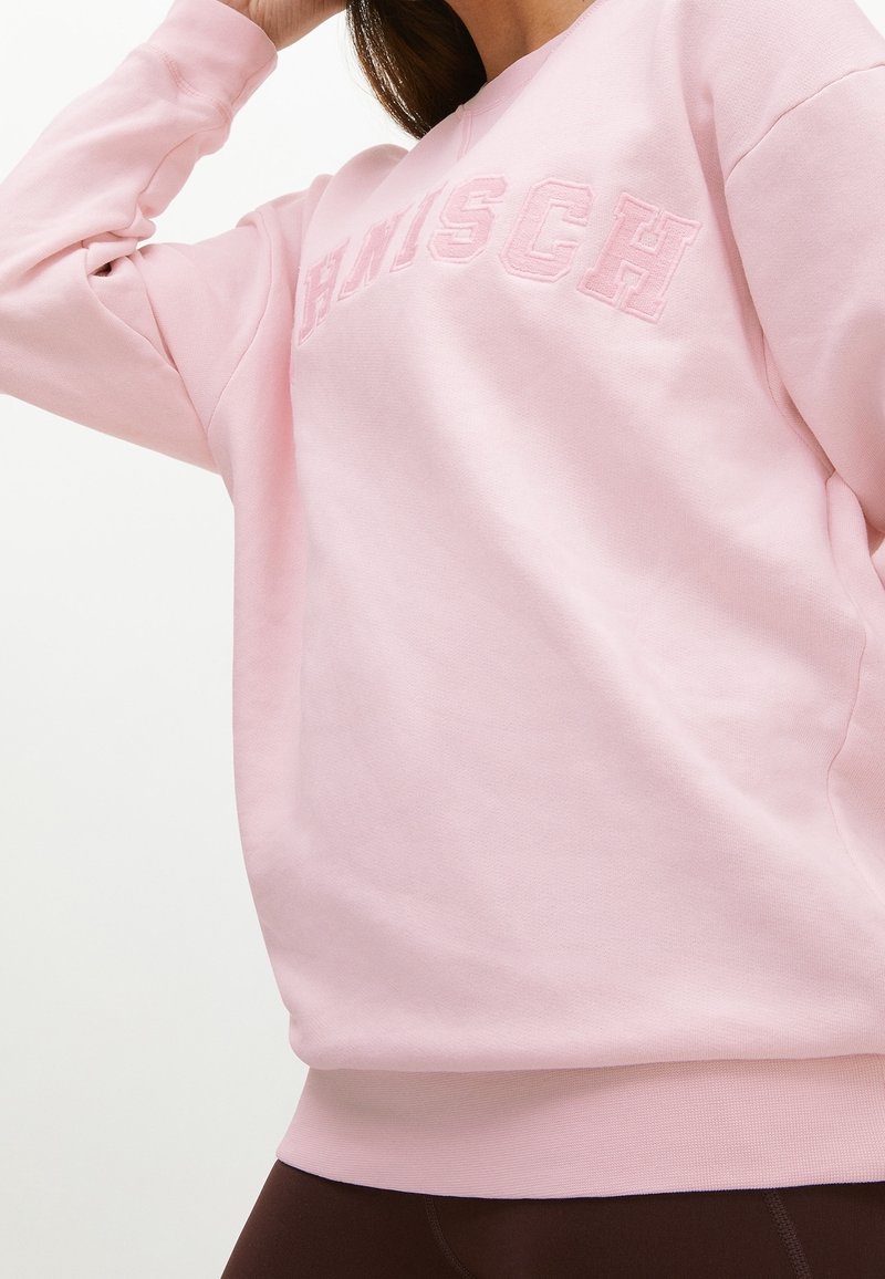 Sweat-shirt rose avec une texture douce et un ourlet côtelé, présentant des lettres brodées en relief sur le devant. Manches longues et coupe décontractée.