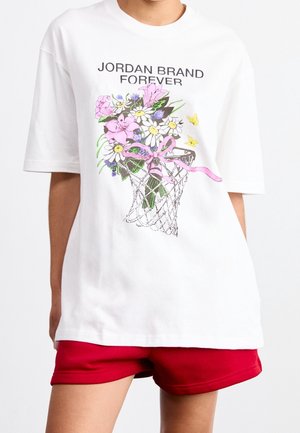 T-shirt blanc avec le texte "JORDAN BRAND FOREVER", un panier de basket tenant un bouquet de fleurs roses et blanches, porté avec un short rouge.