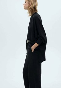 Black oversized top with long sleeves and a relaxed fit, paired with loose black trousers. Texture appears soft; features a belt detail.