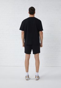 Zwarte katoenen t-shirt met korte mouwen en een relaxte pasvorm, gecombineerd met bijpassende zwarte shorts. Model draagt witte sportschoenen.