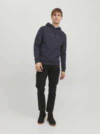 Marineblå hoodie med en front kangaroo-lomme og guld logo-tekst. Kombination med sorte jeans og sorte sko med brune såler.