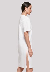 Weißes Baumwoll-T-Shirt-Kleid mit kurzen Ärmeln, Rundhalsausschnitt und seitlichen Schlitzen. Glatte Textur, knielang, minimalistisches Design.