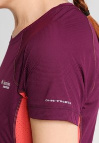 Lila idrottströja i strukturerat tyg, med orange detaljer och en logo med texten "OMNI-FREEZE" på ärmen.