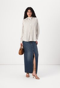 Camicia a righe beige chiaro con strisce navy, abbinata a una lunga gonna di jeans con uno spacco frontale, accessoriata con una borsa marrone.