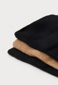 Trois bonnets en tricot empilés : deux en noir et un en beige. Texture côtelée, matériau doux, avec un design replié au niveau de la bordure.