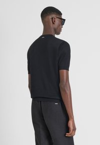 Maglione nero a maglia con maniche corte, scollo rotondo, forma aderente e dettaglio discreto sull'etichetta posteriore, abbinato a pantaloni neri.