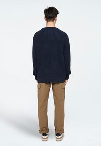 Navyblauwe gestructureerde trui met een kabelbreipatroon, gedragen over khaki cargo broek. De trui heeft een ruime halslijn en geribbelde manchetten.