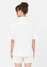 Camicetta bianca a maniche corte con una vestibilità rilassata, caratterizzata da un colletto classico e tessuto in cotone morbido, abbinata a pantaloni corti coordinati.
