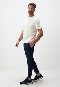 Witte T-shirt met korte mouwen gecombineerd met navy slim-fit broek. De broek heeft zijzakken en het model draagt zwarte sneakers.