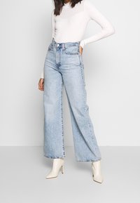 Ljusblå, vida denimjeans har hög midja och subtila blekningar. Parat med en vit ribbad långärmad topp och beige klackboots.