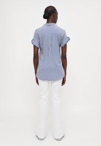 Blauw-witte gestreepte shirt met opgerolde korte mouwen, achterste yoke en relaxte pasvorm, gecombineerd met witte flare-pantalons.