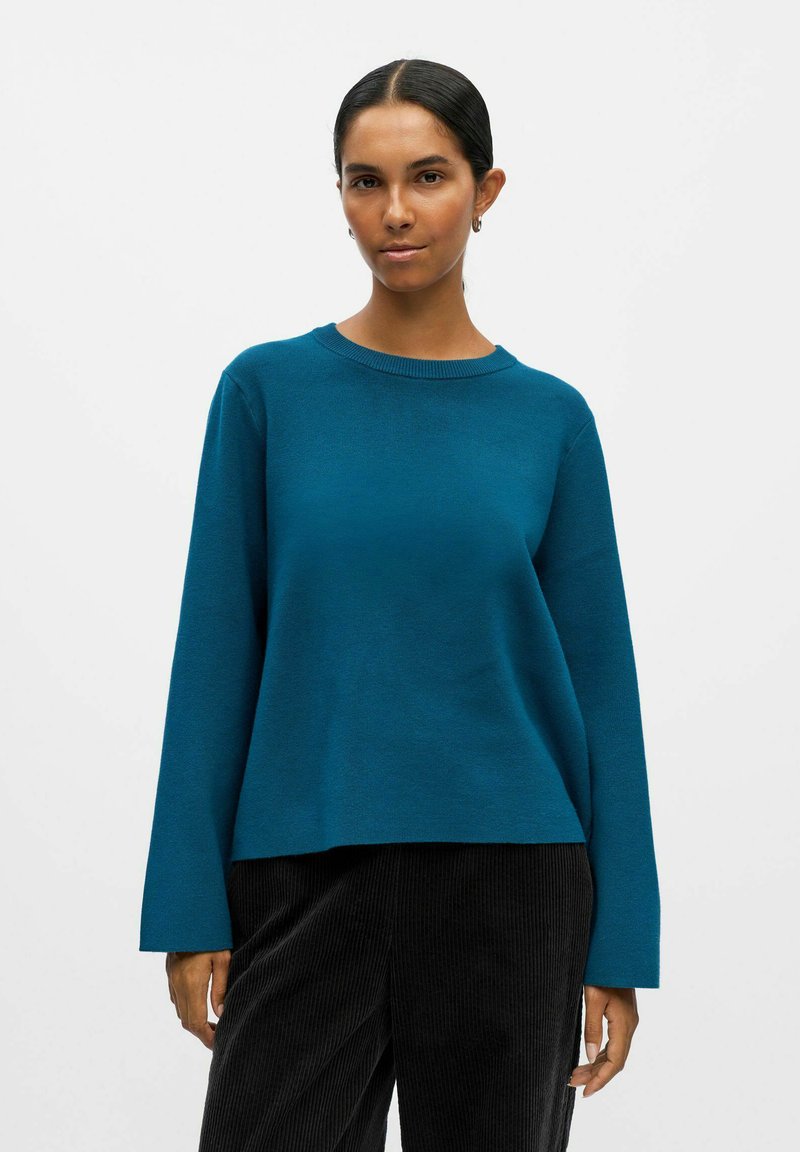 Teal långärmad tröja med rund hals, med en slät textur och avslappnad passform. Matchad med mörka kordbyxor.