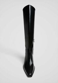 Botte en cuir noir, haute jusqu'au genou, avec un bout pointu, une texture lisse, un design élancé et un détail de fermeture éclair sur le côté.