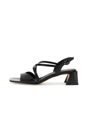 Sandalo aperto in pelle nera con cinturini incrociati, cinturino alla caviglia con fibbia rotonda e tacco medio a blocco su sfondo bianco.