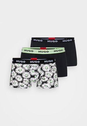 Tri páry boxeriek: jedny čierne s bielym logom, jedny so zeleným pásom a jedny s kvetinovým čierno-bielym vzorom so zelenými akcentmi.