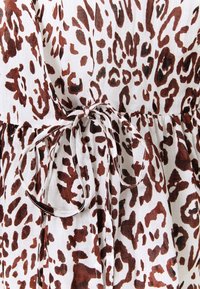 Tissu blanc avec un motif léopard irrégulier marron et un nœud noué à la taille créant des fronces sur le vêtement.