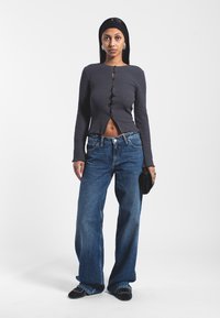Gray ribbed top with decorative buttons, paired with high-waisted wide-leg blue jeans. Model holds a black clutch bag.