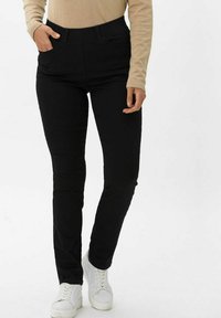 Pantaloni neri slim-fit con una texture liscia, dotati di vita media, tasche frontali e un design elegante, abbinati a sneakers bianche.