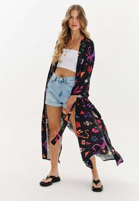 Dlouhý černý kimono s barevnými vzorovými designy, lehká tkanina, otevřený přední díl a dlouhé rukávy, nošené přes bílé crop top a šortky.