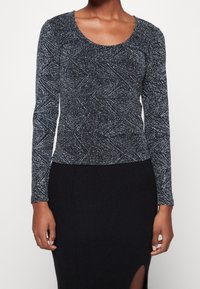 Zwarte top met lange mouwen en een textuurdesign met zilveren spikkels. Ronde halslijn en aansluitende silhouet, gecombineerd met een geribde zwarte rok.