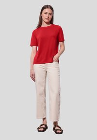 Červené tričko s krátkým rukávem vyrobené z měkké tkaniny, v kombinaci s krémovými širokými džíny a černými sandály s úpravou ve vzoru želvoviny.