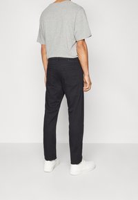 Pantalones negros de corte regular, confeccionados en algodón, combinados con una camiseta de manga corta gris claro, llevados con zapatillas blancas.