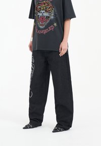 Svart oversized t-shirt med färggrafisk tiger, som kombineras med mörka denimbyxor med vita detaljer och spetsiga svarta skor.