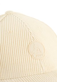 Crème corduroy pet met ribbelstructuur, voorzien van een opvallende lichtgekleurde rubberen logo patch met het woord "JOTT."