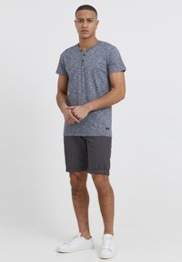 Grå melert kortermet henley-skjorte med tre-knappsfeste, kombinert med mørkegrå shorts og hvite sneakers. Avslappet stil.
