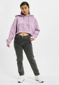 Korte lavendelkleurige hoodie met een capuchon en trekkoorden, gecombineerd met hoge, donkere jeans en witte sportschoenen.