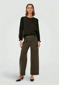 Čierna blúzka s dlhým rukávom a okrúhlym výstrihom v kombinácii s olivovo zelenými nohavicami s vysokým pásom a širokými nohami. Celý outfit dopĺňajú čierne lodičky.