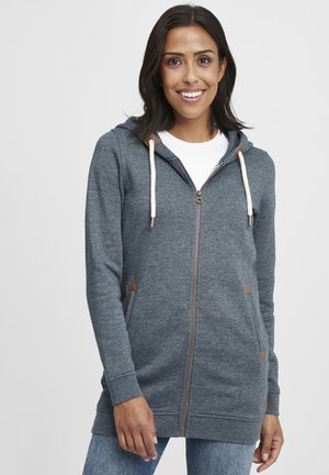 Sweat à capuche zippé en tissu gris foncé, avec des cordons crème, des accents marron au niveau des poches, et une coupe décontractée avec un design à mi-longueur.