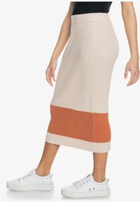Jupe midi en maille côtelée beige avec une bande horizontale orange brûlée contrastante à l'ourlet. Associée à des baskets blanches.