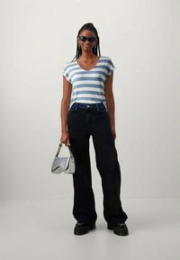 T-shirt de mangas curtas às riscas em azul claro e branco, combinado com jeans escuros de cintura alta. Acessórios incluem uma elegante mala prateada e óculos de sol pretos.