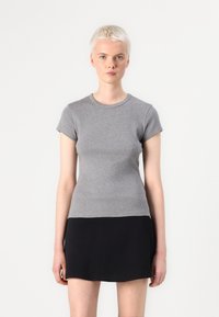 Top grigio a maniche corte realizzato in tessuto leggero, con scollatura rotonda e design aderente, abbinato a una gonna nera elasticizzata.