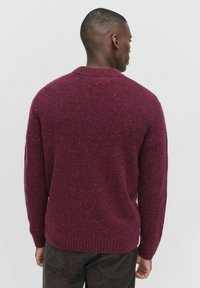 Chunky gebreide trui in diep bordeaux met gestructureerde spikkels. Rib gebreide manchetten en onderrand. Klassiek crew neck ontwerp.