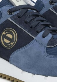 Atletická teniska s vrchní částí z námořnického semiše a síťoviny, texturovanými akcenty a gumovou podrážkou se vzorem proti skluzu. Viditelný detail loga.