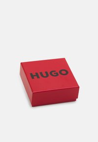 Red rectangular box with a glossy finish, featuring a prominent black "HUGO" logo on the lid. Compact design with squared corners.