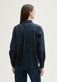 Navy shirt with textured dot patterns, long sleeves, and a collar. Made from lightweight fabric, features a straight hem and button cuffs.