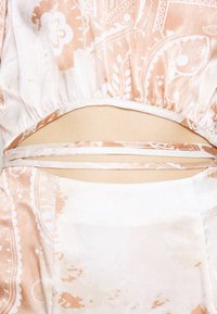 Gros plan de la taille montrant un tissu à motifs pêche clair et blanc avec un design découpé et des liens fins en tissu sur la peau.