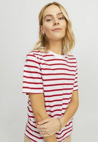 T-shirt de manga curta listrado em branco e vermelho, com decote redondo e textura de algodão suave. Modelo de braços cruzados.