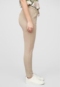 Beige leggings laget av mykt stoff, med snor i midjen og en tettsittende silhuett. Kombinert med hvite joggesko.