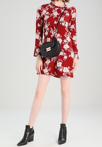 Rotes Blumen-Langarmkleid mit weißen Mustern, kombiniert mit einer schwarzen Umhängetasche und schwarzen Knöchelstiefeln. Glatte Textur, moderne Passform.