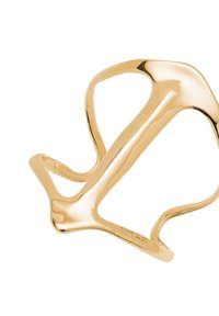Brazalete escultórico de color dorado con líneas suaves y curvas y una forma orgánica. Presenta un acabado pulido y elementos de diseño distintivos y fluidos.