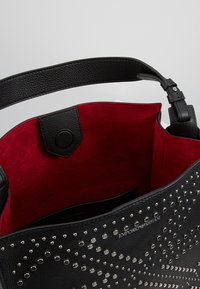 Czarna skórzana torebka z czerwonym zamszowym wnętrzem, zdobiona srebrnymi ćwiekami w układzie wzorów. Regulowany pasek i zapięcie na zatrzask.