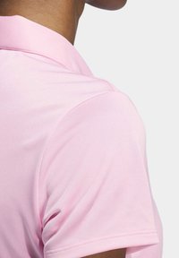 Gros plan d'une personne portant un polo à manches courtes rose clair, montrant la zone de l'épaule et du col.