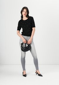 Pull court noir à manches courtes avec des accents en perles, jeans skinny gris clair, sac à main noir et escarpins noirs à bout pointu. Texture lisse sur toute la surface.