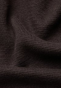 Ciemnobrązowa dzianina o widocznej fakturze splotu oraz miękkie fałdy tworzące cienie i refleksy światła.